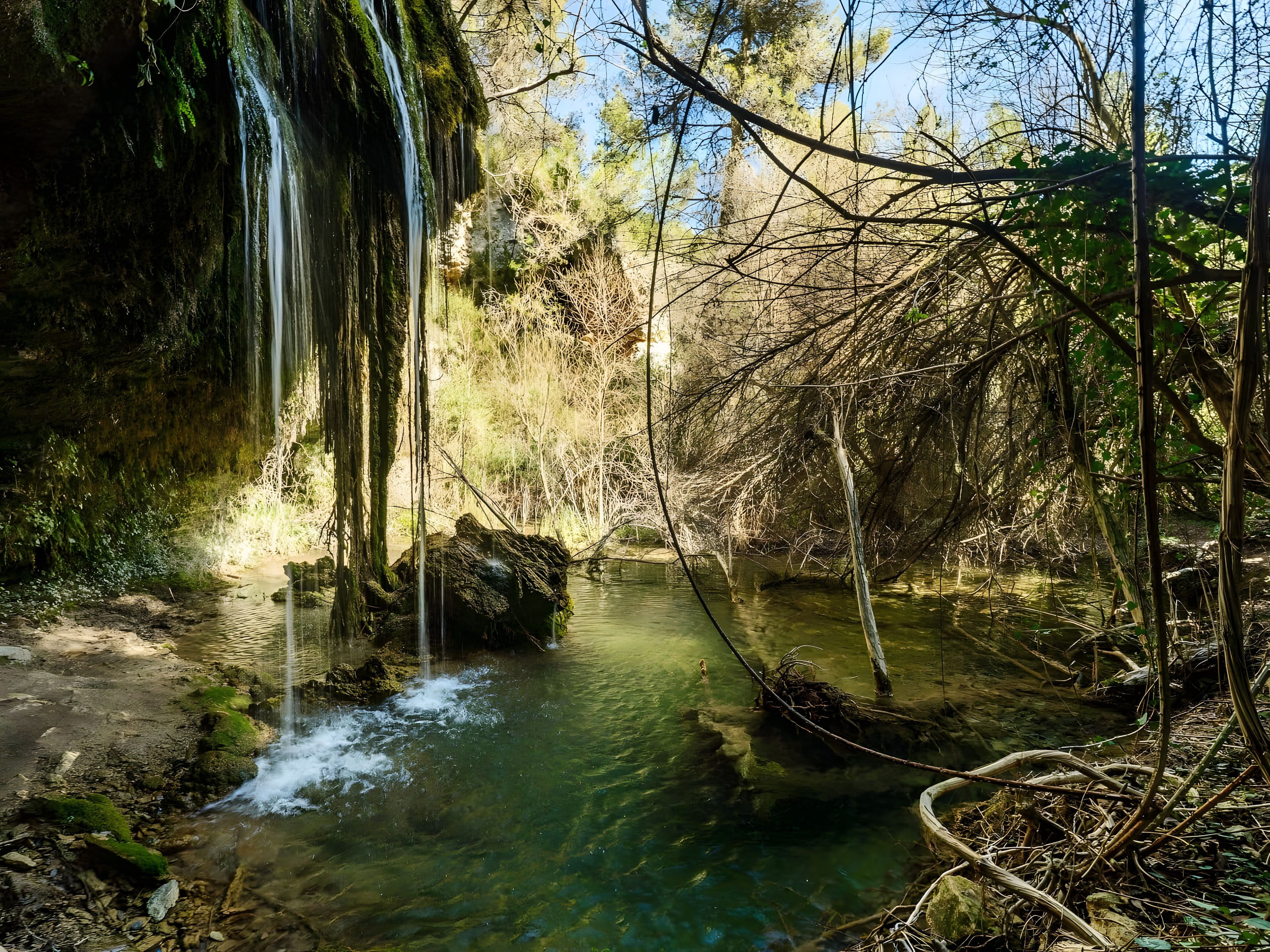 Een natuurlijk landschap met een waterval, helder water en omliggende begroeiing.