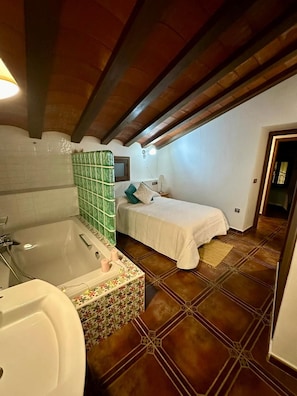Un dormitorio con una cama individual, una mesita de noche, una lámpara y un baño con bañera y lavamanos.