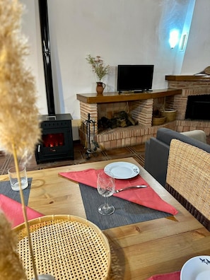 Una sala de estar acogedora con chimenea, televisor y comedor, con una mesa, sillas y un florero.