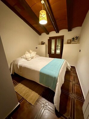Un dormitorio con cama, lámpara colgante, ventana y puerta.