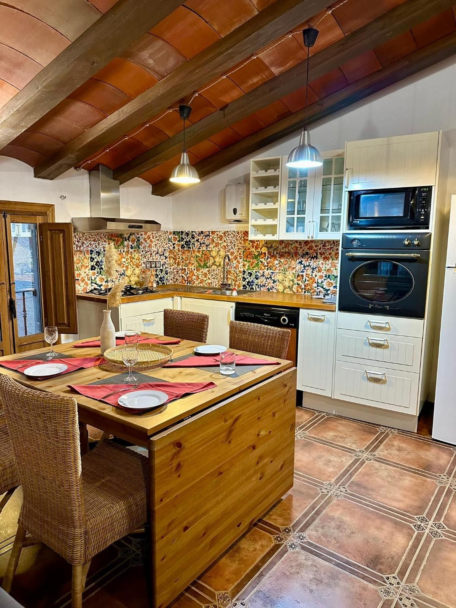 Una cocina con una mesa de madera lista para comer, armarios blancos y salpicadero de azulejos.