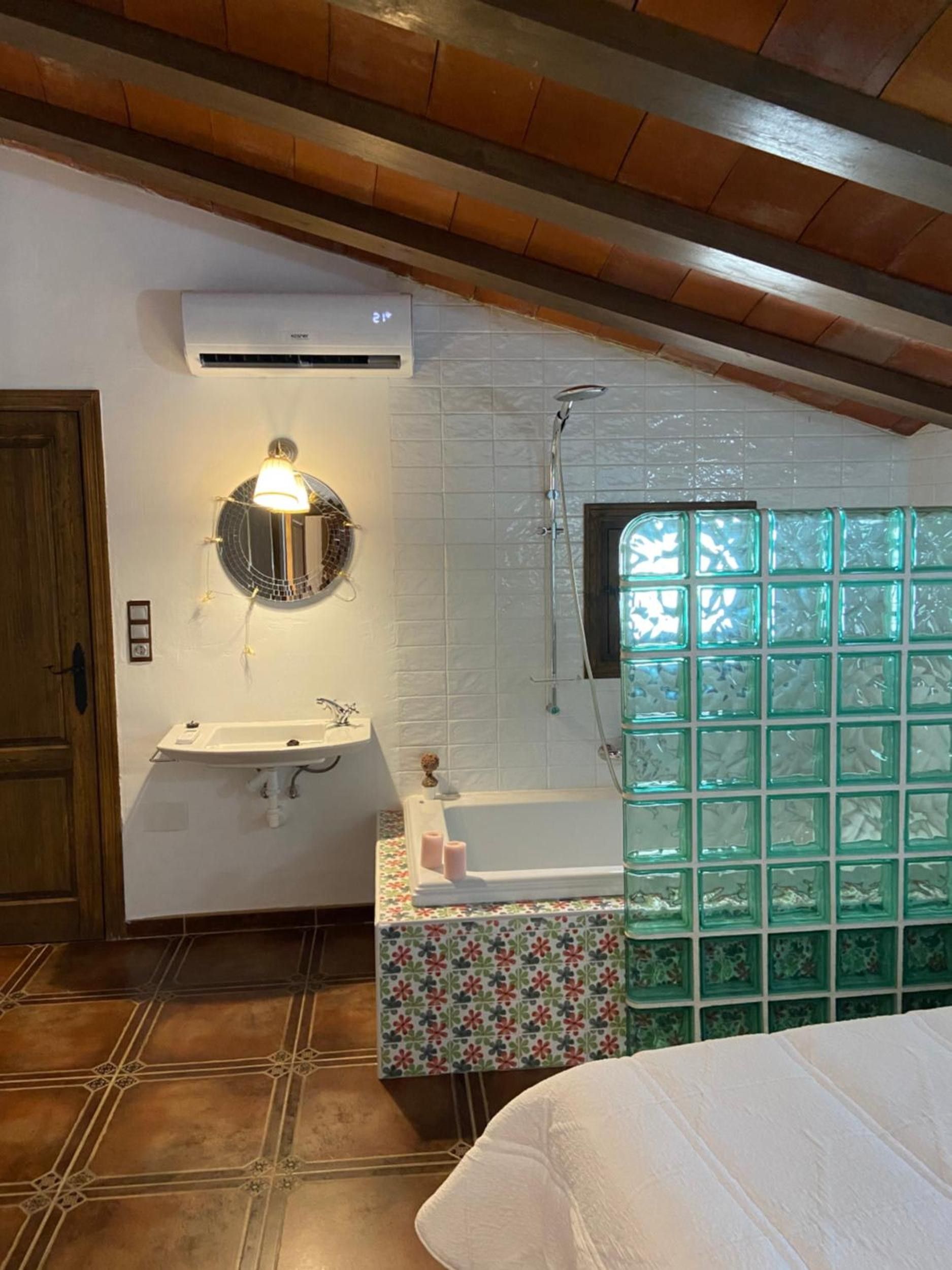 Un baño con un lavamanos blanco, un espejo redondo, una ducha y una ventana con bloques de vidrio verde.