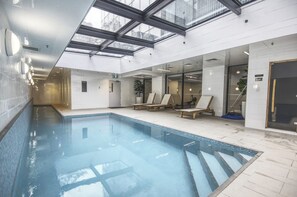 Une piscine int érieure avec des parois en verre transparent, un sol carrelé et une verrière au-dessus.