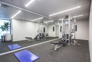 Ein Fitnessraum mit Trainingsgeräten, einem großen Spiegel und einer blauen Matte.