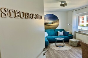 Ein Zimmer mit einem blauen Sofa, einem runden Couchtisch und einem an der Wand hängenden Landschaftsbild.
