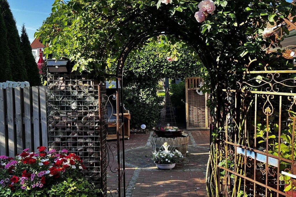 A garden with a metal gate, a wooden fence, and a brick pathway.