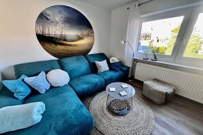 Een moderne woonkamer met een blauwgroene bank, een ronde salontafel en een groot abstract schilderij aan de muur.