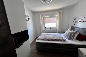 Een slaapkamer met een bed, een raam met gordijnen, een wanddecoratie en een radiator.