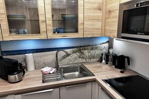 A kitchen with wooden cabinets, a stainless steel sink, a coffee maker, and a built-in oven. - Holiday apartment with 2 bedrooms (Langeoog)