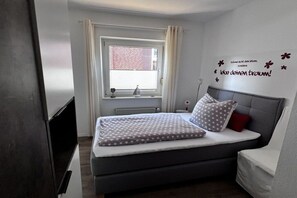 Ein Schlafzimmer mit einem Bett, einem Fenster mit Vorhängen, einer Wanddekoration und einem Nachttisch.