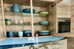 A kitchen with wooden cabinetry, glass shelves, and a built-in oven. - Holiday apartment with 2 bedrooms (Langeoog)