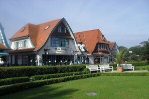A traditional building with a restaurant sign, a covered outdoor seating area, and a well-maintained garden with benches. - Holiday apartment with 2 bedrooms (Boltenhagen)