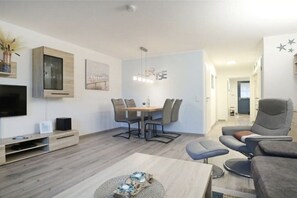 A modern living room with a dining area, a flat-screen TV, and a seating arrangement. - Holiday apartment with 2 bedrooms (Boltenhagen)