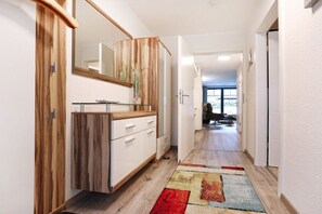 Ein Flur mit einem Holzschrank, einem Waschbecken mit Glasplatte und einem farbenfrohen Teppich.