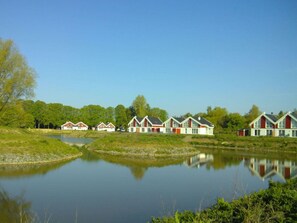 A row of red and white houses with a calm lake in the foreground. - Holiday Home in Nordhorn With Swimming Pool (Nordhorn)
