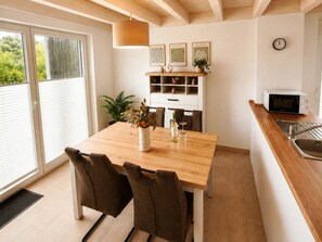 A modern kitchen with a wooden table, two chairs, a microwave, and a sink. - Holiday Home in Nordhorn With Swimming Pool (Nordhorn)