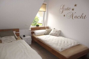 Une chambre avec deux lits simples, une table de chevet, une commode et une fenêtre donnant sur un beau paysage.