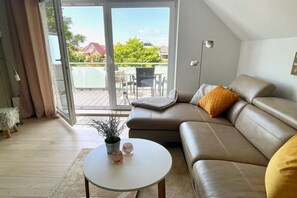 A modern living room with a leather sofa, a small round table with a plant, and a view of a balcony with outdoor furniture. - Holiday apartment with 2 bedrooms (Norddeich)