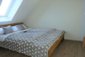 Ein Schlafzimmer mit schrägem Dach, einem Bett mit sterngestreckter Bettdecke und einem Holzkopfende.