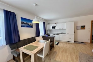 A modern living room with a dining table, a sofa, and a kitchen area with white cabinets and a microwave. - Holiday home in Turnau with swimming pool (Turnau)