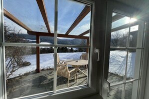 A covered patio with a table and chairs, a wooden pergola, and a view of a snowy landscape.
