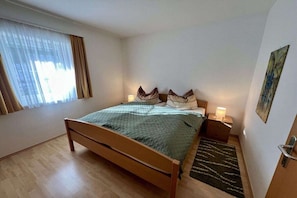 A bedroom with a wooden bed, a nightstand with a lamp, a window with curtains, and a painting on the wall. - Holiday home in Turnau with swimming pool (Turnau)