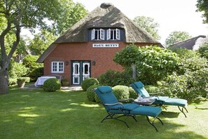 Ein reetgedecktes Haus namens 'Haus Betty' mit gepflegtem Rasen und zwei Liegestühlen.
