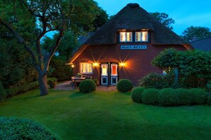 Una casa tradizionale con tetto di paglia, chiamata 'Haus Betty', con un giardino curato e un'area salotto esterna ben visibile.