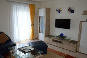 A modern living room with a glass coffee table, a black sofa, a glass-topped TV stand, and a wardrobe. - Haus Thon Superior Apartment (Bodensdorf)