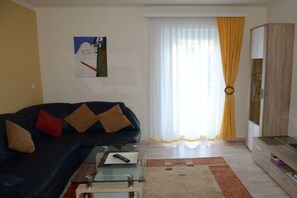 A living room with a sofa, a glass coffee table, a painting on the wall, a window with curtains, and a cabinet. - Haus Thon Superior Apartment (Bodensdorf)