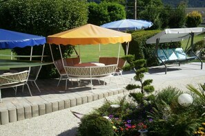 A patio area with a round table and chairs under a yellow canopy, a blue canopy, and a white canopy. - Haus Thon Superior Apartment (Bodensdorf)
