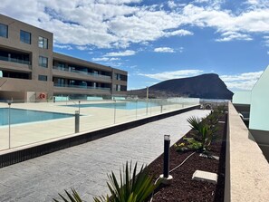 A modern building with a pool area, a lifebuoy, and a mountain in the background. - Vacation Apartment 'Sotavento Suites' with Sea View, Shared Pool and Wi-Fi (El Médano)