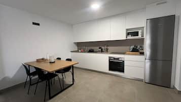 A modern kitchen with white cabinets, a wooden dining table, black chairs, a stainless steel refrigerator, and a microwave.