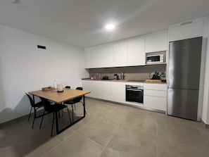 A modern kitchen with white cabinets, a wooden dining table, black chairs, a stainless steel refrigerator, and a microwave. - Vacation Apartment 'Sotavento Suites' with Sea View, Shared Pool and Wi-Fi (El Médano)
