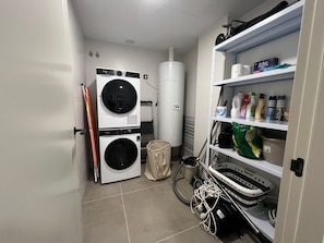 A laundry room with two stacked washing machines, a dryer, and a shelf with cleaning supplies. - Vacation Apartment 'Sotavento Suites' with Sea View, Shared Pool and Wi-Fi (El Médano)