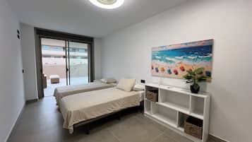 A hotel room with two beds, a ceiling fan, a painting of a beach scene, and a small plant on a console table.