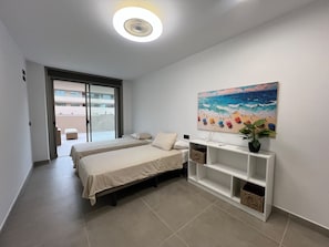 Ett hotellrum med två sängar, en takfläkt, en tavla som föreställer en strandscen och en liten växt placerad på ett sidobord.