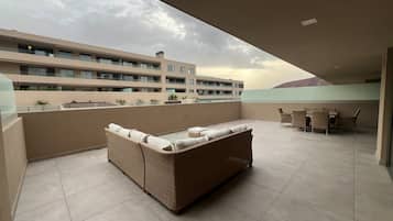 A rooftop terrace with a wicker sofa and a dining set.