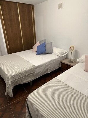 A bedroom with two beds, a nightstand, a lamp, and a wardrobe.