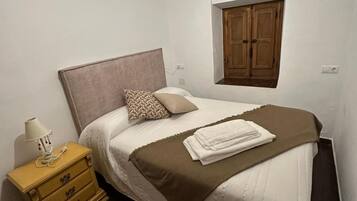 Un dormitorio con cama, mesita de noche, lámpara, ventana con persiana de madera y una lámpara de pared.