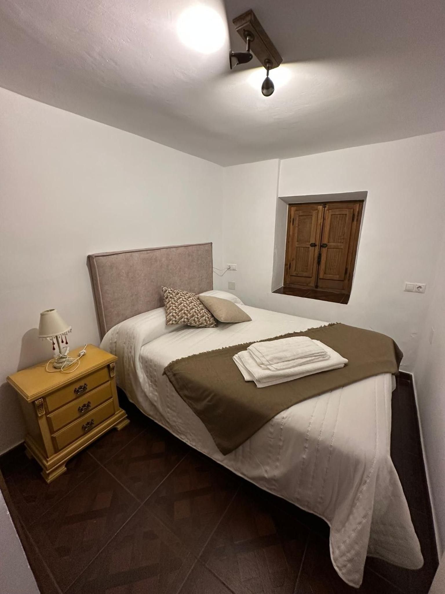 Un dormitorio con una cama, una mesita de noche, una lámpara, un armario de madera y una ventana.