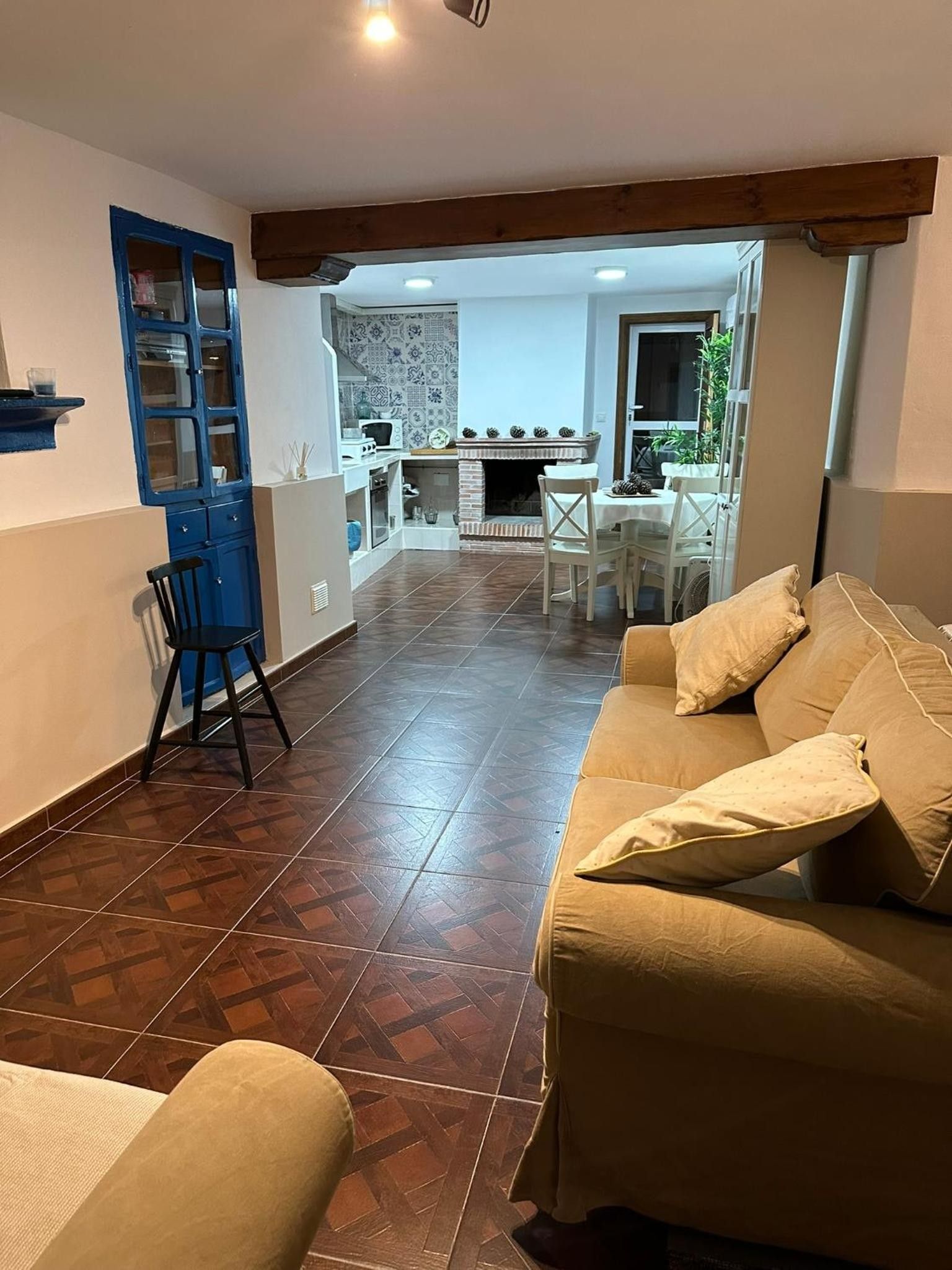 Una sala de estar con sofá, un comedor con mesa y sillas, una cocina con estufa y alacenas, y un mueble azul con puertas de vidrio.