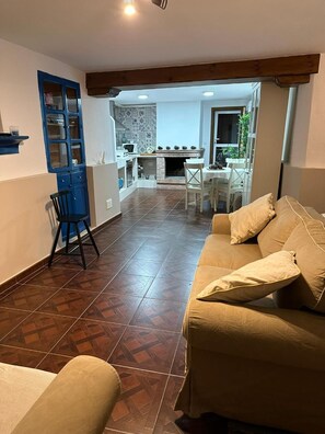 A living room with a sofa, a dining area with a table and chairs, a kitchen area with a stove and cabinets, and a blue cabinet with glass doors.