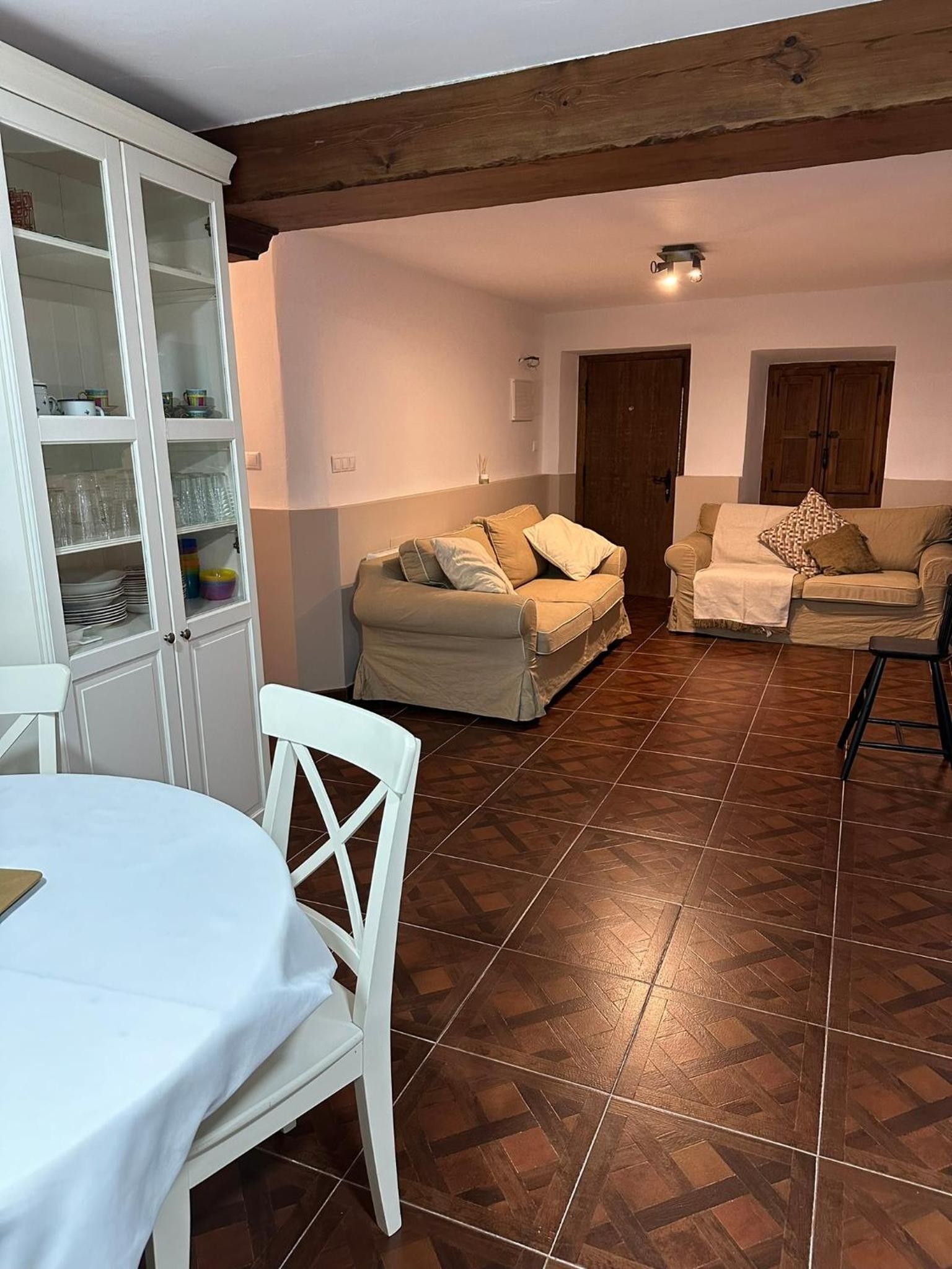 Una sala de estar con una mesa de comedor, dos sofás y un aparador con puertas de cristal.