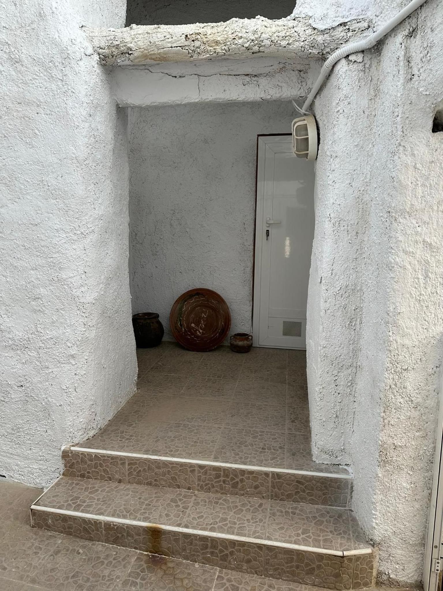 Un escalier étroit menant à une porte, avec un sol carrelé et un mur à texture.