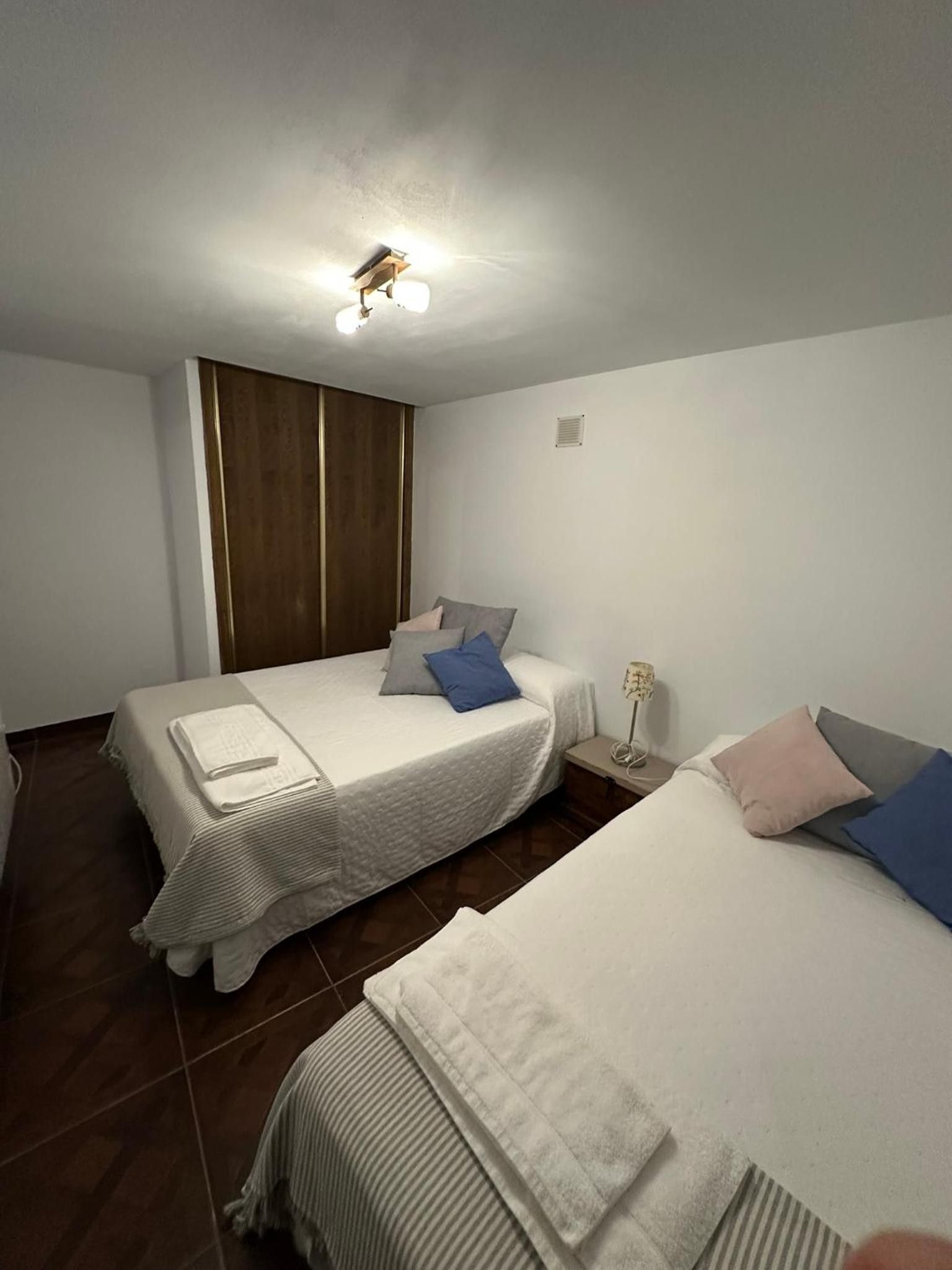Habitación de hotel con dos camas, un armario de madera, una mesita de noche con lámpara y un aplique de techo.