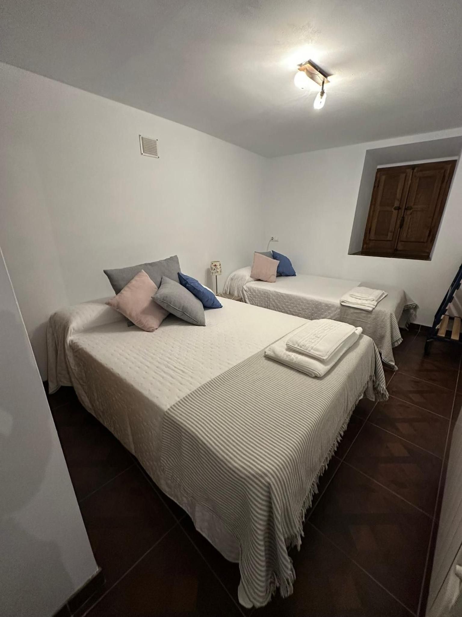 Una habitación con dos camas, una lámpara en el techo, una ventana y un armario de madera.