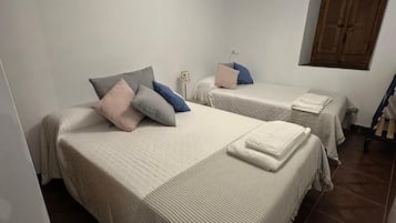 Una habitación con dos camas, una lámpara en el techo, una ventana y un armario de madera.