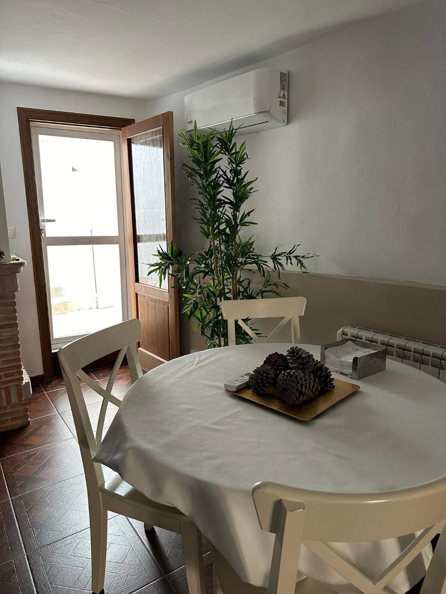 Un comedor con una mesa redonda, sillas blancas, una planta en maceta y un radiador.
