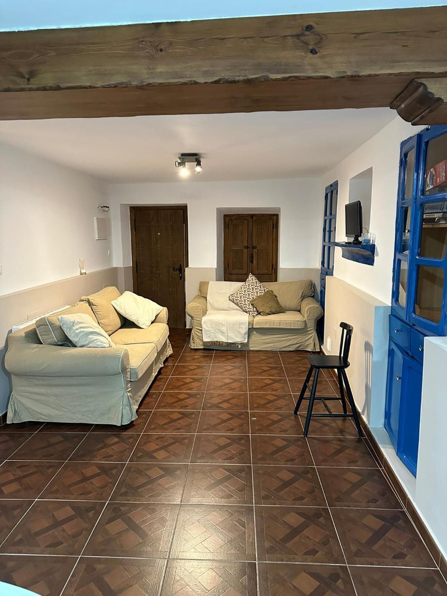 A living room with two sofas, a coffee table, and a TV. There are wooden doors and a blue cabinet.